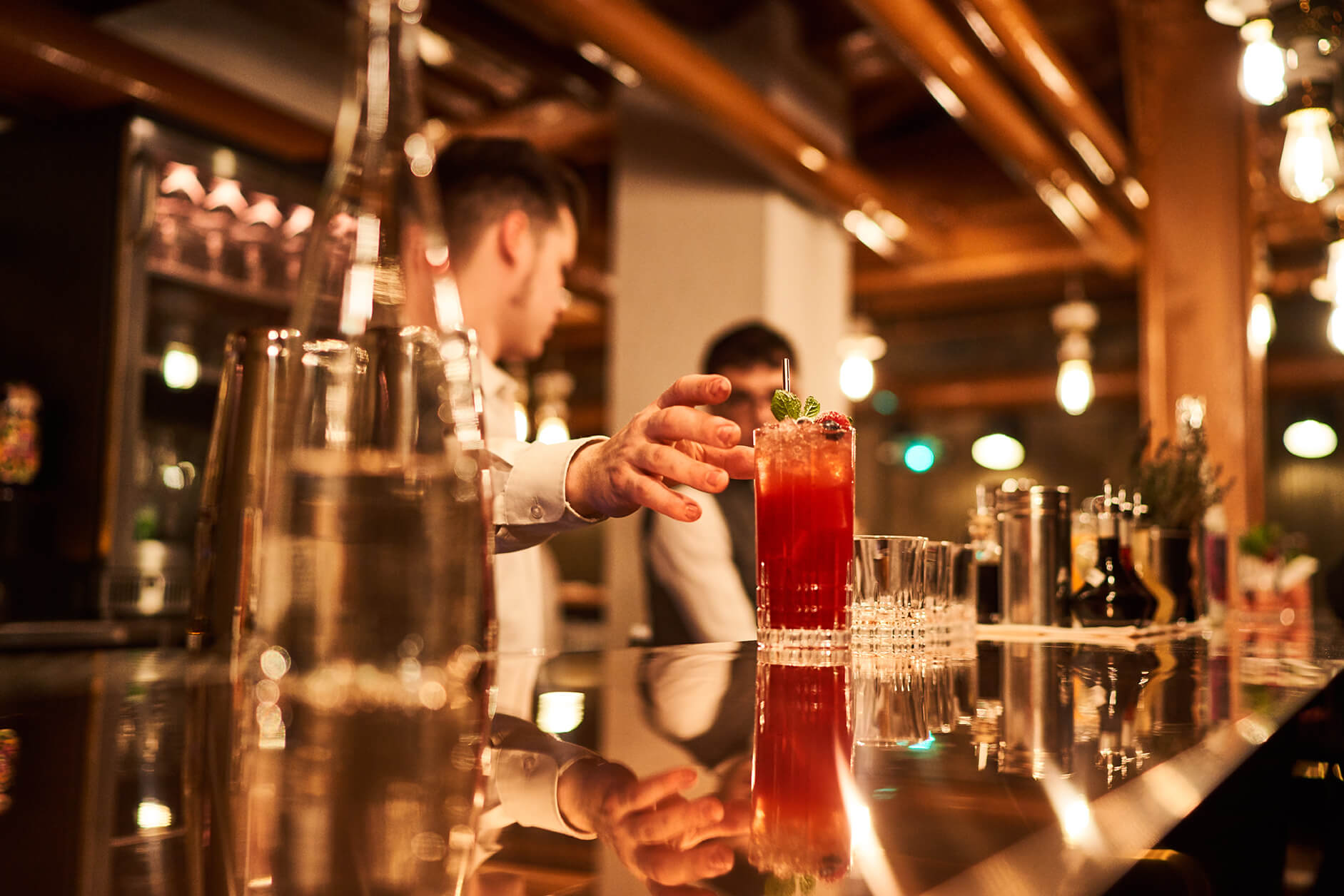 Serveur attrapant un cocktail rouge sur un bar.